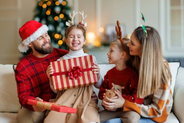 Sevimli mutlu küçük çocuklar Noel hediyeleri alırken genç ve sevgi dolu ebeveynlerle oturuyorlar.