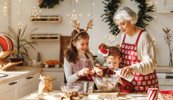 Zwei kleine Kinder backen gemeinsam mit der Großmutter in der Küche selbst gebackene Weihnachtsplätzchen — Stockfoto