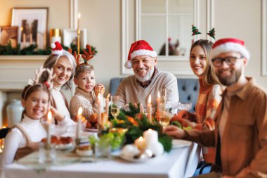 Noel Baba şapkalı mutlu bir aile yemek masasında gülümsüyor ve kameraya bakıyor.