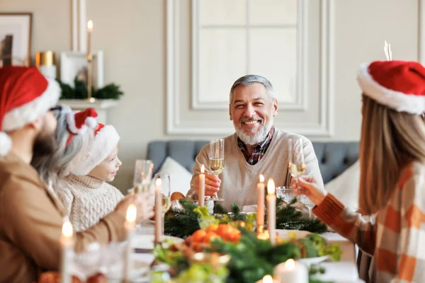 Glad flera generationer familj i Santa hattar vid middagsbordet, säger jul rostat bröd och klinkande glasögon — Stockfoto