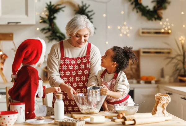 Feliz multirracial niños ayudan a la abuela a cocinar galletas de Navidad en la cocina durante las vacaciones de invierno —  Fotos de Stock
