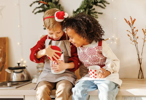 Два взволнованных счастливых многорасовых детей мальчики открывают металлическую банку с традиционным рождественским печеньем на кухне — стоковое фото