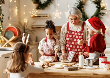 Çok ırklı bir aile, büyükanne ve üç küçük çocuk mutfakta birlikte Noel kurabiyesi pişiriyorlar.