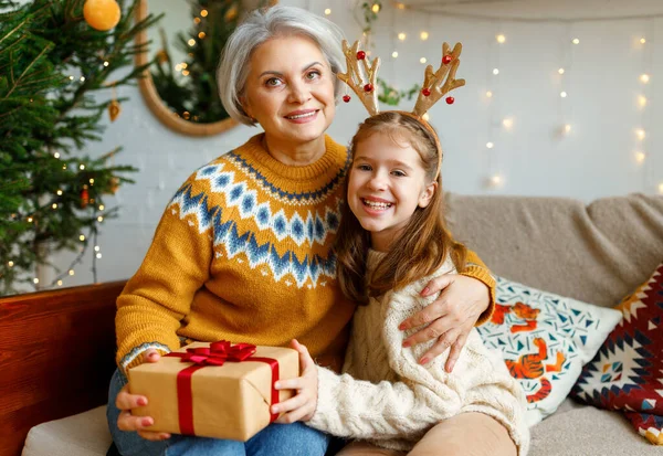 Mała wnuczka daje świąteczne pudełko uśmiechniętej babci podczas ferii zimowych — Zdjęcie stockowe