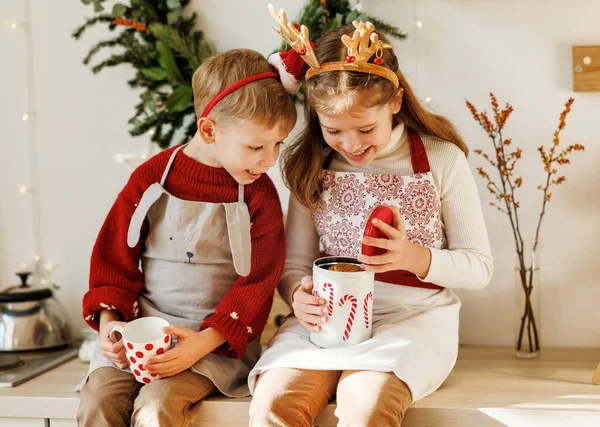 Lindos niños felices sentados en la encimera en la acogedora cocina casera con lata de metal llena de galletas de Navidad — Foto de Stock