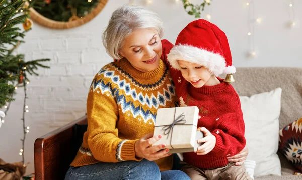 Nieto pequeño dando caja de regalo de Navidad a la abuela sonriente durante las vacaciones de invierno — Foto de Stock