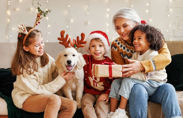 Gelukkig multi-etnische familie, grootmoeder met kleinkinderen en hond genieten van kerstdag — Stockfoto