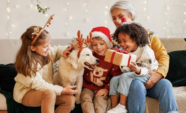 Gelukkig multi-etnische familie, grootmoeder met kleinkinderen en hond genieten van kerstdag — Stockfoto