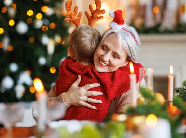 Nieto pequeño abrazando feliz abuela sonriente durante la cena de Navidad en casa —  Fotos de Stock