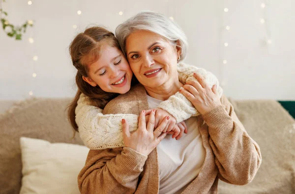 Cute happy little girl granddaughter hugging delighted elderly grandmother during Christmas holidays — Stock Photo, Image