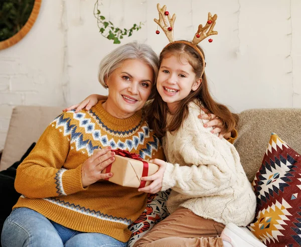 Little girl granddaughter giving Christmas gift box to smiling grandmother during winter holidays — Stock Photo, Image