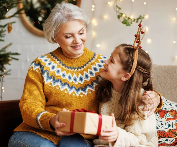 Menina neta dando caixa de presente de Natal à avó sorridente durante as férias de inverno — Fotografia de Stock