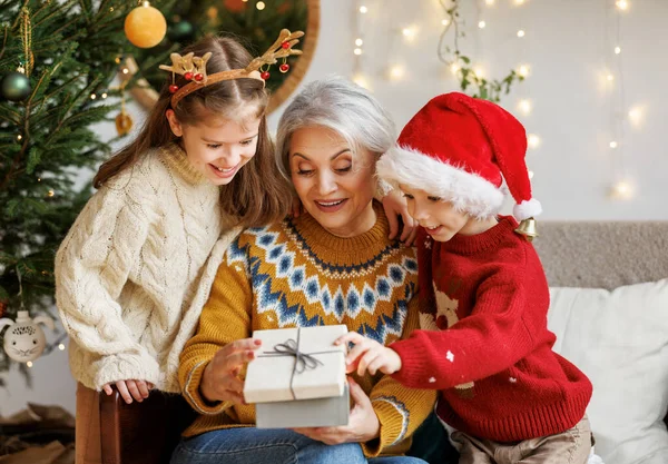 Små barn barnbarn och sonson ger julklapp låda till leende mormor under vintern semester — Stockfoto