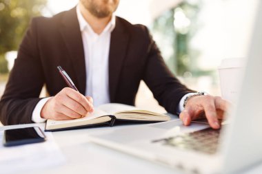 Takım elbiseli bir iş adamının açık hava kafedeki dizüstü bilgisayarla uzaktan çekilmiş görüntüsü.