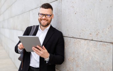 Takım elbiseli neşeli işadamı dışarıda beklerken online toplantı sırasında tablet web kamerasına el sallıyor. 