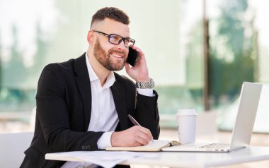 Gülümseyen işadamı açık kafede cep telefonuyla keyifli sohbetler yapıyor.