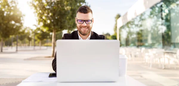 Glad ung manlig lärare i hörlurar sitter framför laptop utanför har lektion på nätet — Stockfoto