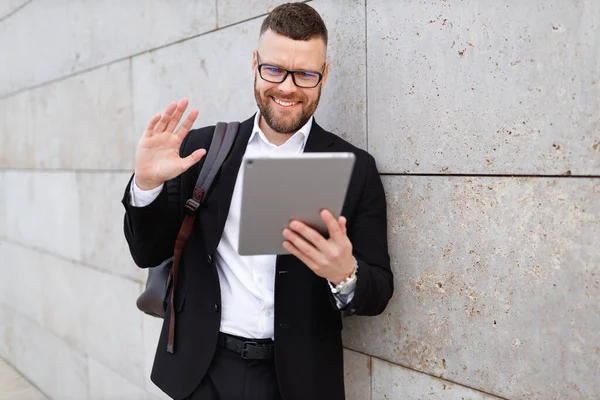 在线会议期间，穿着西服的快乐商人站在外面向平板电脑的摄像头挥手 — 图库照片