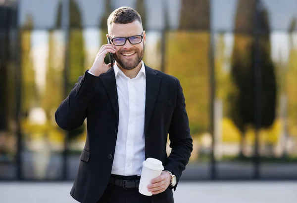 밖에 있는 행복 한 사무직 근로자가 손에 커피를 들고 휴대폰으로 이야기하는 모습 — 스톡 사진