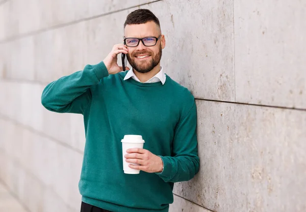 Joven empleado de oficina feliz fuera hablando por teléfono móvil con llevar café en la mano —  Fotos de Stock