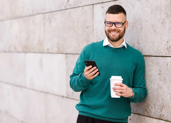 Glimlachende jonge kantoormedewerker in casual kleding buiten staan met mobiele telefoon — Stockfoto