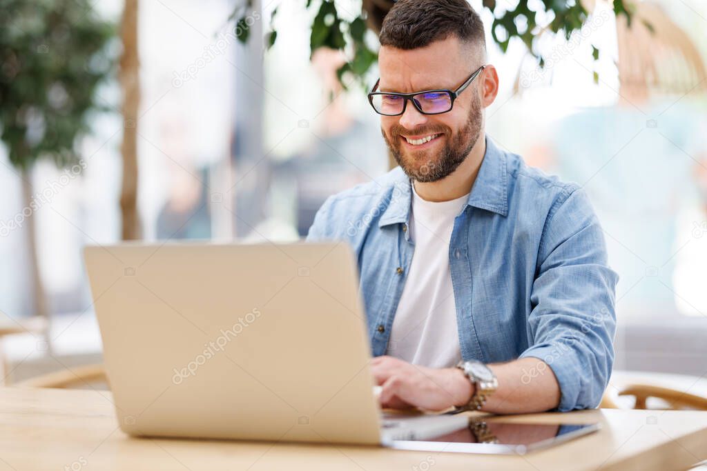 Happy young male businessman sitting in front of laptop outside working and having video conferencing online