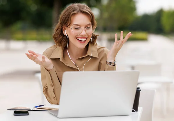 Jovem professor feliz em roupa formal e óculos dando aula on-line sentado com laptop fora — Fotografia de Stock