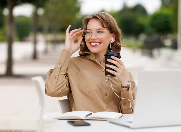 Linda menina estudante em óculos sentado com laptop e xícara de café takeaway fora no terraço — Fotografia de Stock