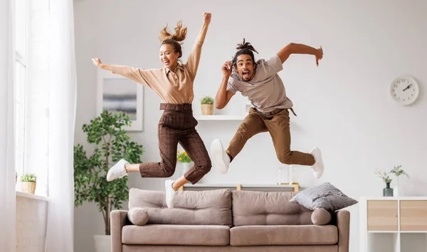 Молодая энергичная активная африканская семейная пара, прыгающая на диване, развлекающаяся вместе дома — стоковое фото