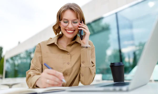 Happy young office assistant working remotely online sitting with laptop and coffee outside — Stock Photo, Image