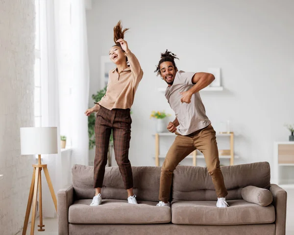 Jovem alegrada casal familiar afro-americano dançando a música no sofá em casa — Fotografia de Stock