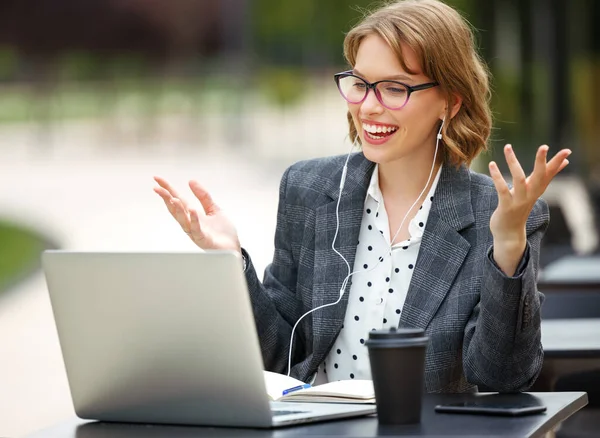 Happy young teacher in formal outfit and glasses giving lesson online sitting with laptop outside — Stock Photo, Image