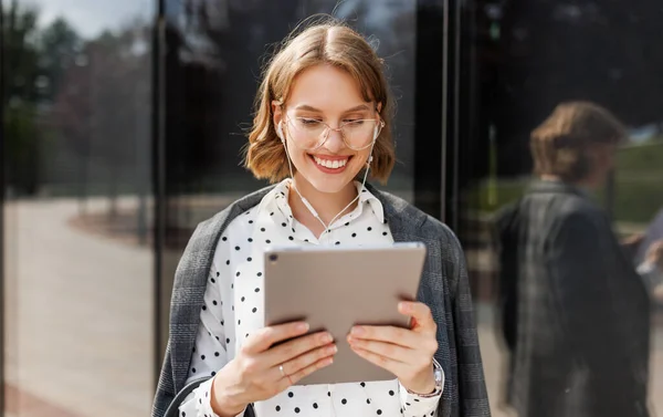 Glada affärskvinna i hörlurar tittar på digital tablett när du står på solig gata utomhus — Stockfoto