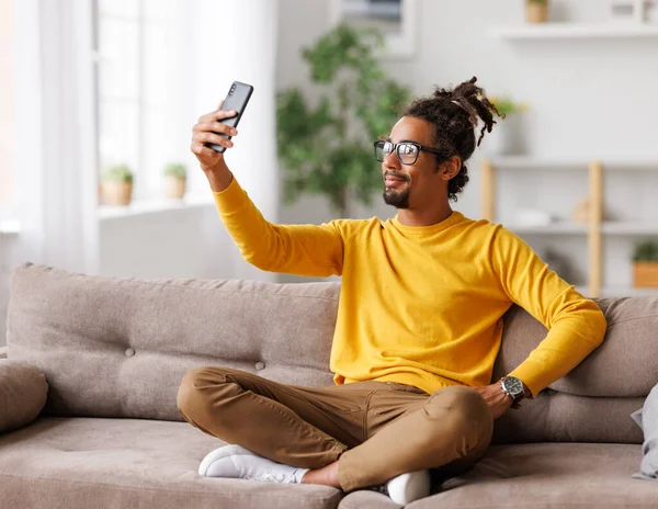 Genç, mutlu, Afro-Amerikan adam koltukta otururken akıllı telefonuyla selfie çekiyor. — Stok fotoğraf