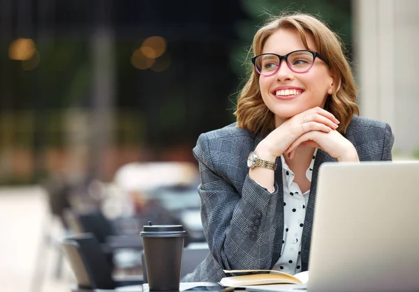 Preciosa mujer de negocios en vasos sentada con portátil y taza de café para llevar al aire libre —  Fotos de Stock