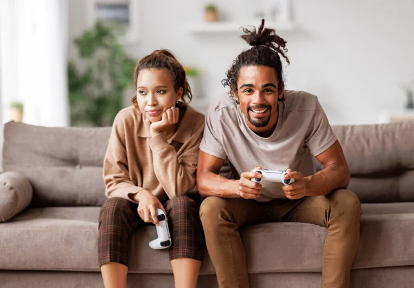 Дата заборгування. Задоволений афроамериканець грає у відеоігри і ігнорує нудну жінку, що сидить поруч. — стокове фото