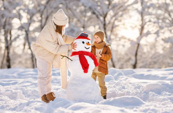 Felice famiglia madre e figlio fare un pupazzo di neve e divertirsi in una passeggiata invernale nel parco — Foto Stock