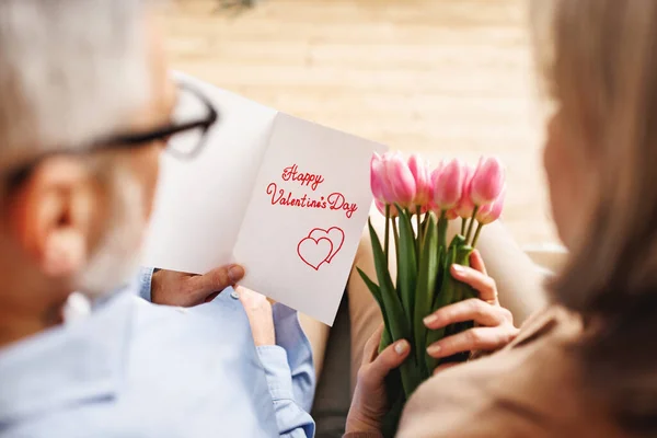 Alla hjärtans dag kort och tulpaner i händerna på ett äldre kärleksfullt par — Stockfoto