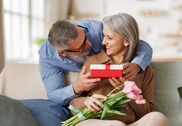 Любящий муж дарит цветы и подарочную коробку на день святого Валентина счастливой удивленной жене — стоковое фото