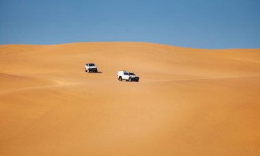 Gezginler kum tepelerinde safaride beyaz arabalara gidiyor.