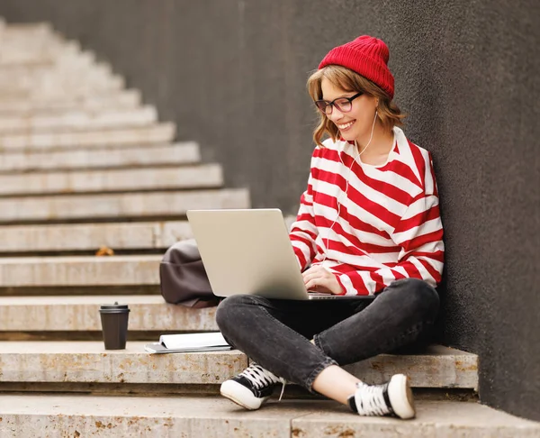 Uśmiechnięta uczennica korzystająca z laptopa siedząc na zewnątrz na klatce schodowej, studiując online Obrazy Stockowe bez tantiem