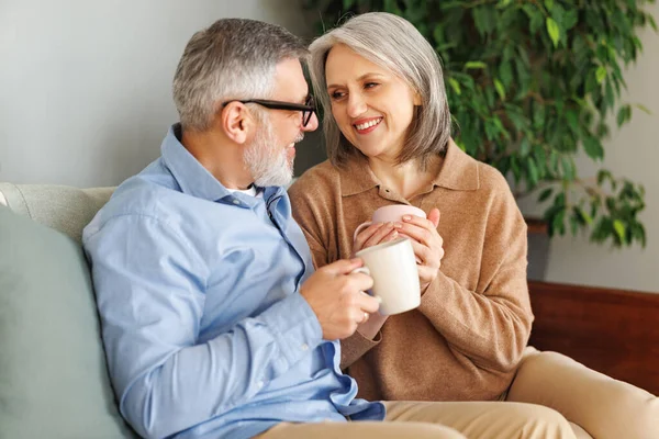 Aimer couple de personnes âgées famille boire du thé et embrasser tout en se relaxant sur un canapé confortable à la maison — Photo