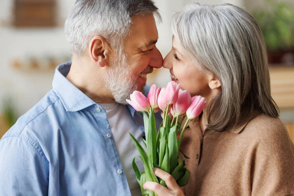 Liebender älterer Mann überreicht Ehefrau Strauß frischer rosa Tulpen zu Hause, gratuliert am 8. März — Stockfoto