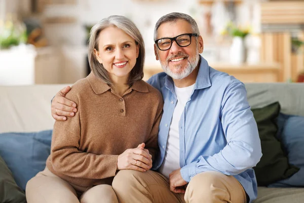 Retrato de feliz pareja de ancianos abrazándose mientras están sentados en el sofá en casa —  Fotos de Stock