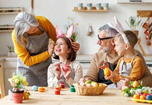 Happy family grandparents and kids enjoying Easter preparation together, coloring eggs in kitchen — Stock Photo, Image