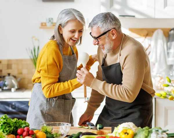 Casal idoso alegre se divertir dançando e cantando enquanto cozinhando juntos na cozinha — Fotografia de Stock