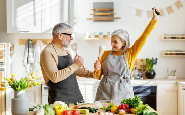 Casal idoso alegre se divertir dançando e cantando enquanto cozinhando juntos na cozinha — Fotografia de Stock