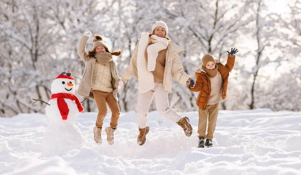 Happy family mother with two little kids holding each others hands and jumping in snowy park — Stock Photo, Image
