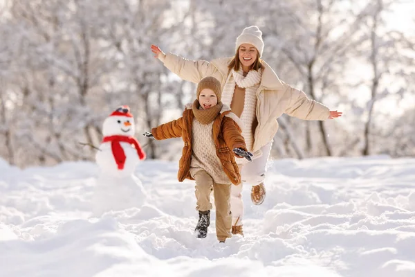 Gelukkige actieve familie moeder en zoontje veel plezier in winterpark, inhalen in besneeuwde dag — Stockfoto