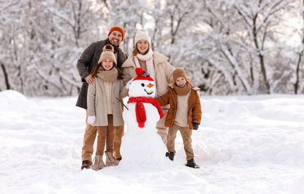 Happy family in warm clothes laughing merrily while making snowman together — Stock Photo, Image